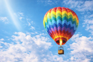 Vibrant Rainbow Hot Air Balloon Flying in Blue Sky Wallpaper - 4K Desktop Background